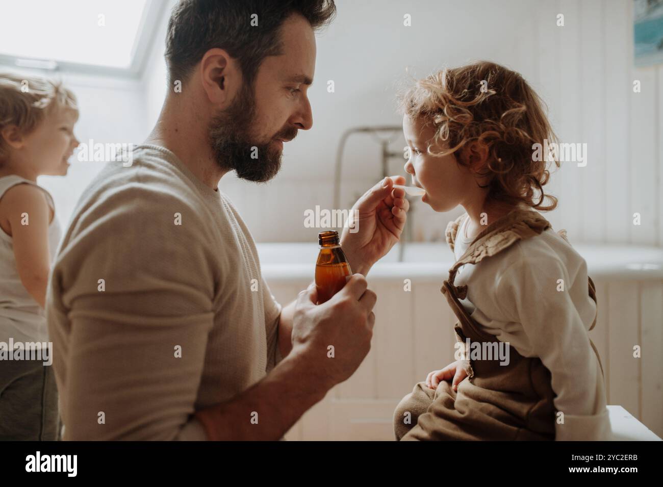 Ragazza malata con febbre e freddo a casa. Padre che dava alla figlia medicine su cucchiaio, sciroppo per tosse o medicina per la febbre. Foto Stock