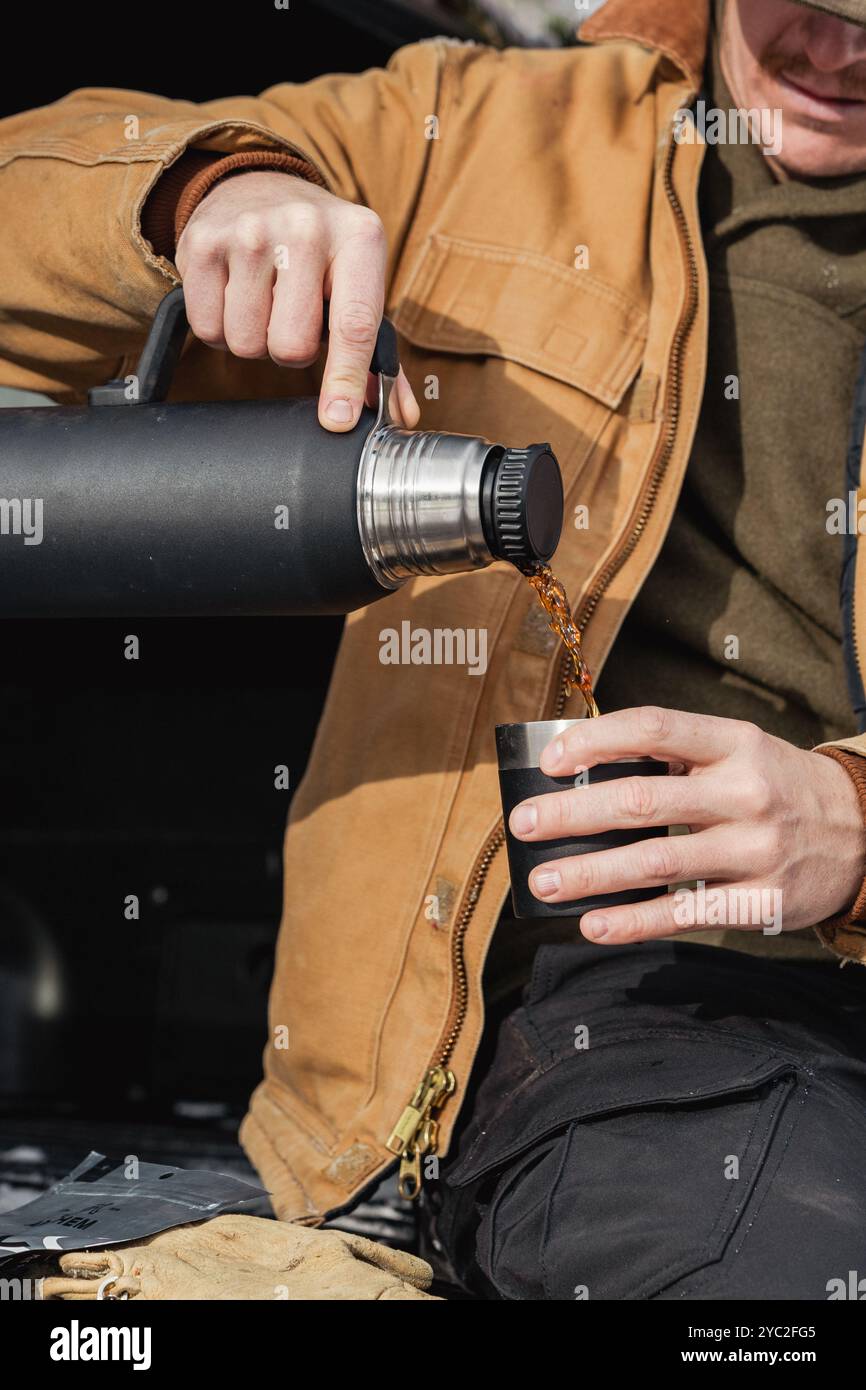 Uomo all'aperto che versa liquido caldo da un thermos in una giornata fredda Foto Stock