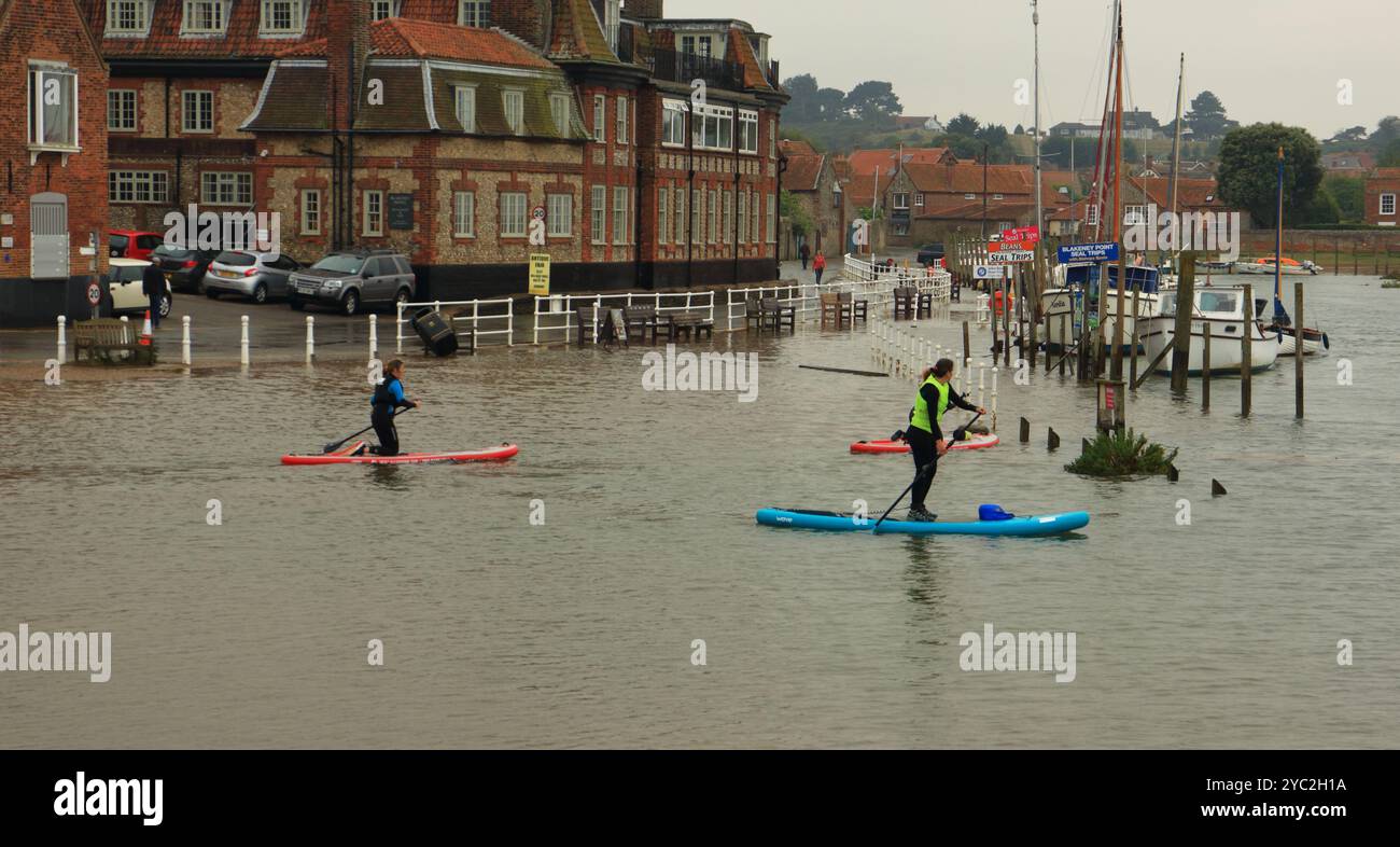 Pagaiate che attraversano il parcheggio allagato fino al canale del porto al culmine di una marea primaverile a Blakeney, Norfolk, Inghilterra, Regno Unito. Foto Stock