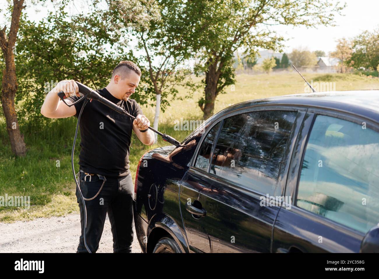 Giovane che tenta di sbloccare una porta auto con uno strumento in un ambiente rurale. Foto Stock