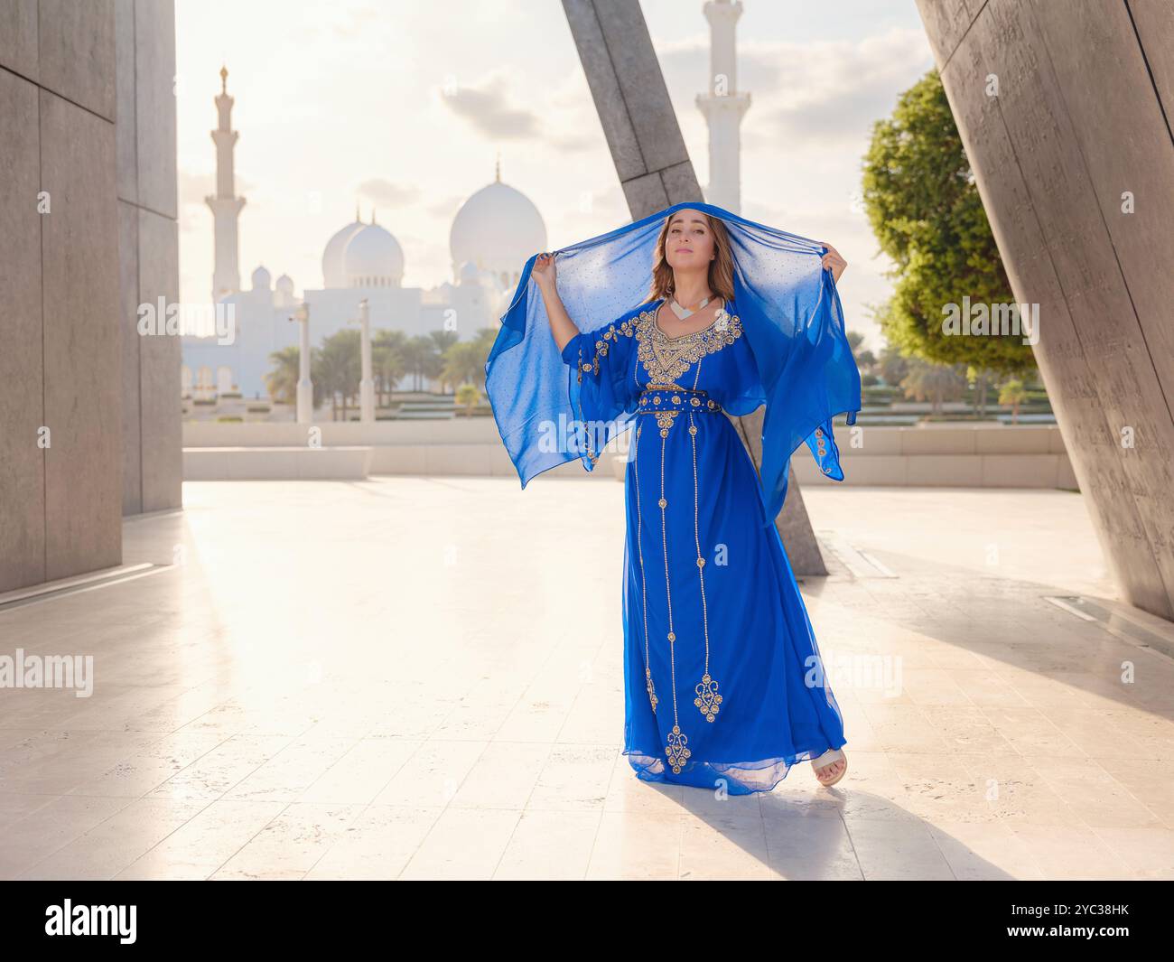 Viaggia verso gli Emirati Arabi Uniti, Abu Dhabi. Donna in abito arabo blu vicino alla grande moschea bianca dello sceicco Zayed. Famosa visita turistica di Abu Dhabi. Foto Stock