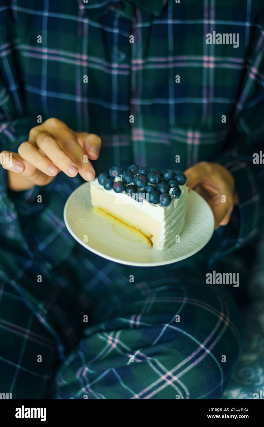 Donna che mangia una Cheesecake in pigiama per un momento di dolce accogliente in camera da letto . Foto di alta qualità Foto Stock