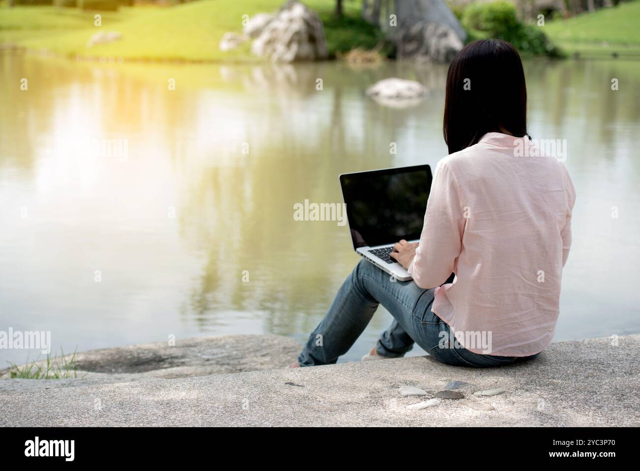 Donna asiatica seduta parco verde con computer portatile. Donna che lavora in un'azienda felice di un notebook che utilizza un notebook con le mani che digitano sulla tastiera Foto Stock