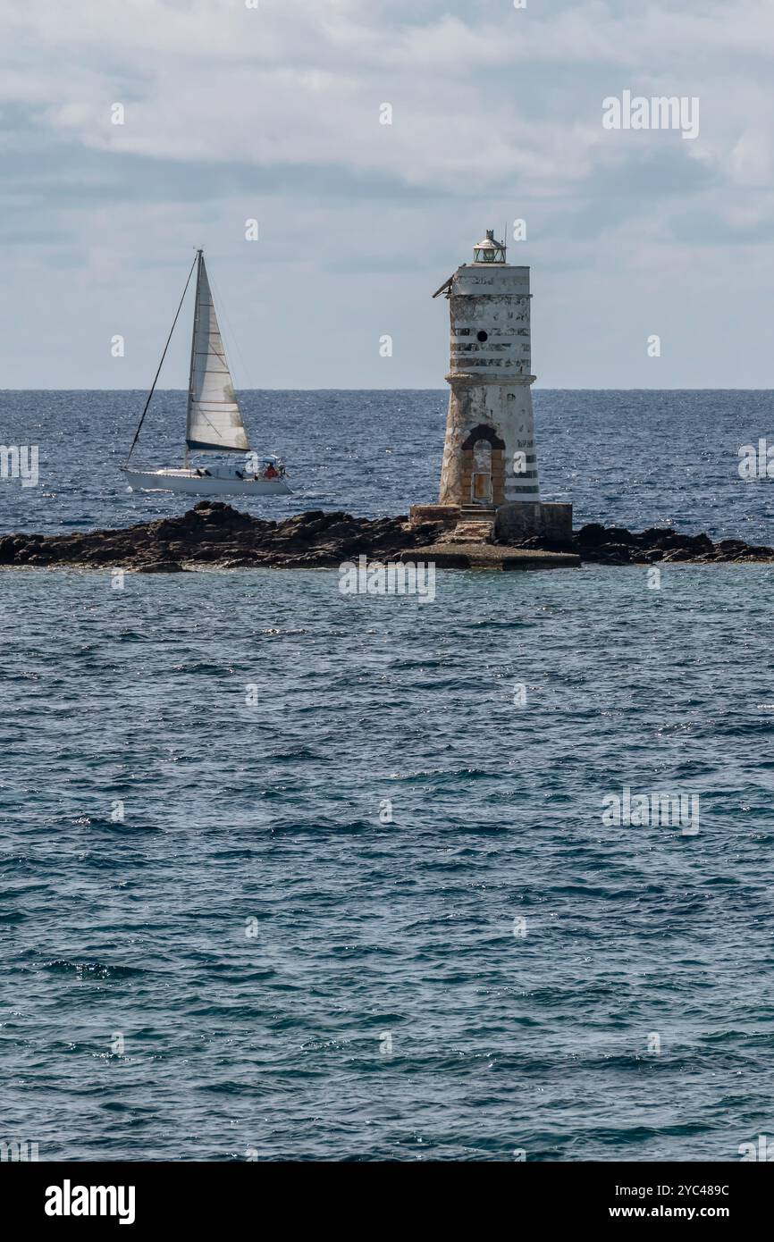 Una barca a vela bianca passa vicino al faro di Mangiabarche, all'isola di Sant'Antioco, in Italia Foto Stock