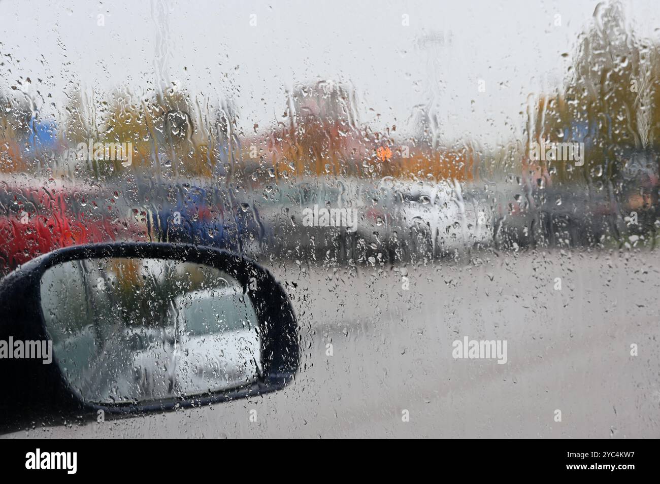 Questa foto cattura una scena di giorno piovoso dall'interno di un'auto, dove le gocce di pioggia si sono accumulate sul parabrezza, offuscando la vista esterna. La sid Foto Stock