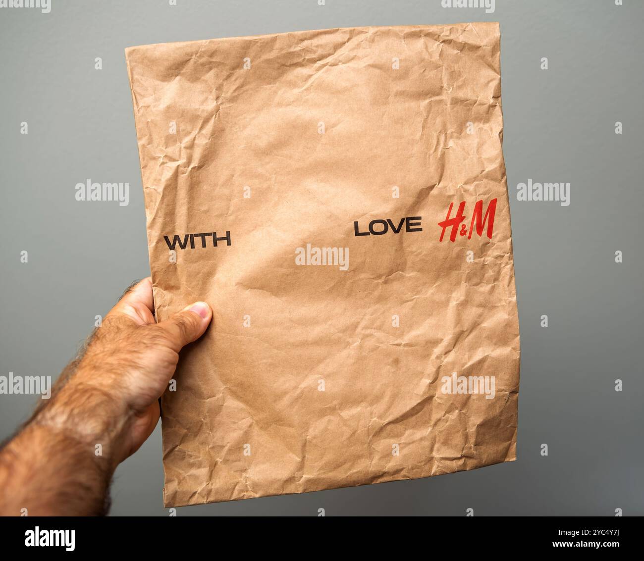 Parigi, Francia - 6 agosto 2024: Una mano regge un sacchetto di carta con le lettere H e M con le parole "H" e "M", che riflette l'approccio minimalista ed eco-consapevole del marchio. Foto Stock