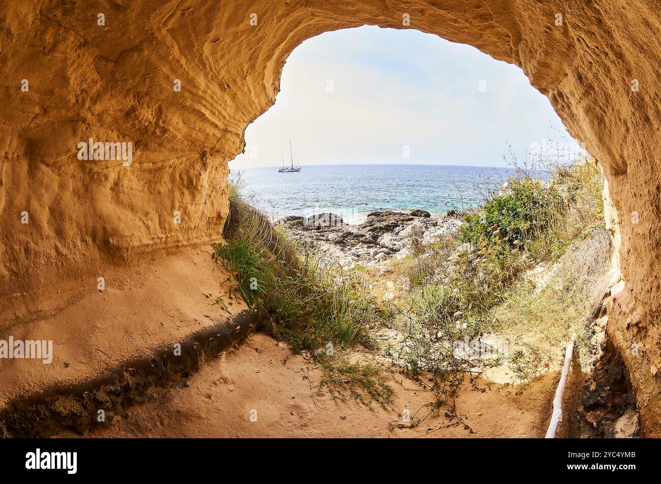 Antico bacino di carenaggio scolpito in arenaria sulla spiaggia di sa Cala e nave a vela sullo sfondo (la Mola, Formentera, Isole Baleari, Mar Mediterraneo, Spagna) Foto Stock