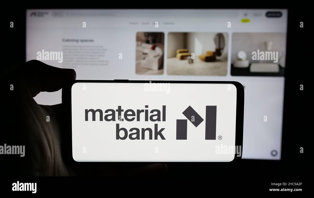 Persona che detiene un cellulare con il logo della società statunitense di materiali campione Material Bank sullo schermo di fronte alla pagina Web aziendale. Mettere a fuoco il display del telefono. Foto Stock