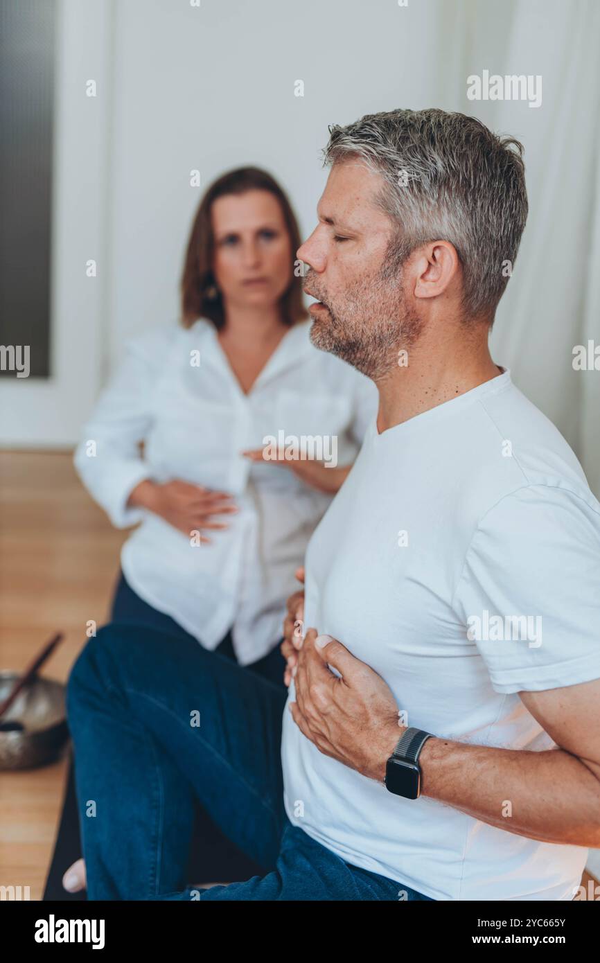 Uomo e donna che praticano la respirazione consapevole insieme durante una sessione di meditazione, seduti su tappeti con ciotole sonore. Foto di alta qualità Foto Stock