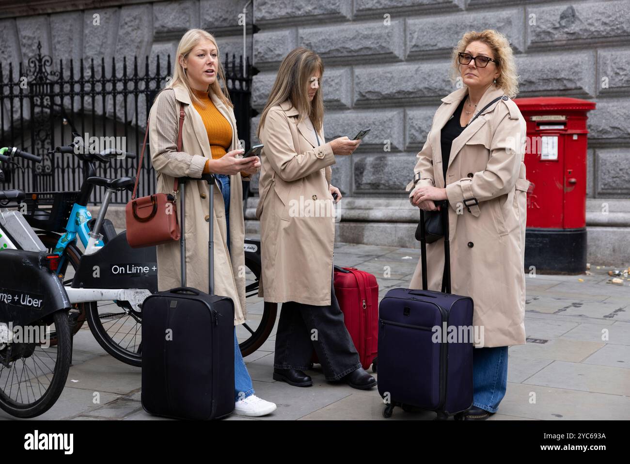 Le signore con impermeabili beige e valigie navigano lungo Fleet Street sui loro smartphone, City of London, Inghilterra, Regno Unito Foto Stock