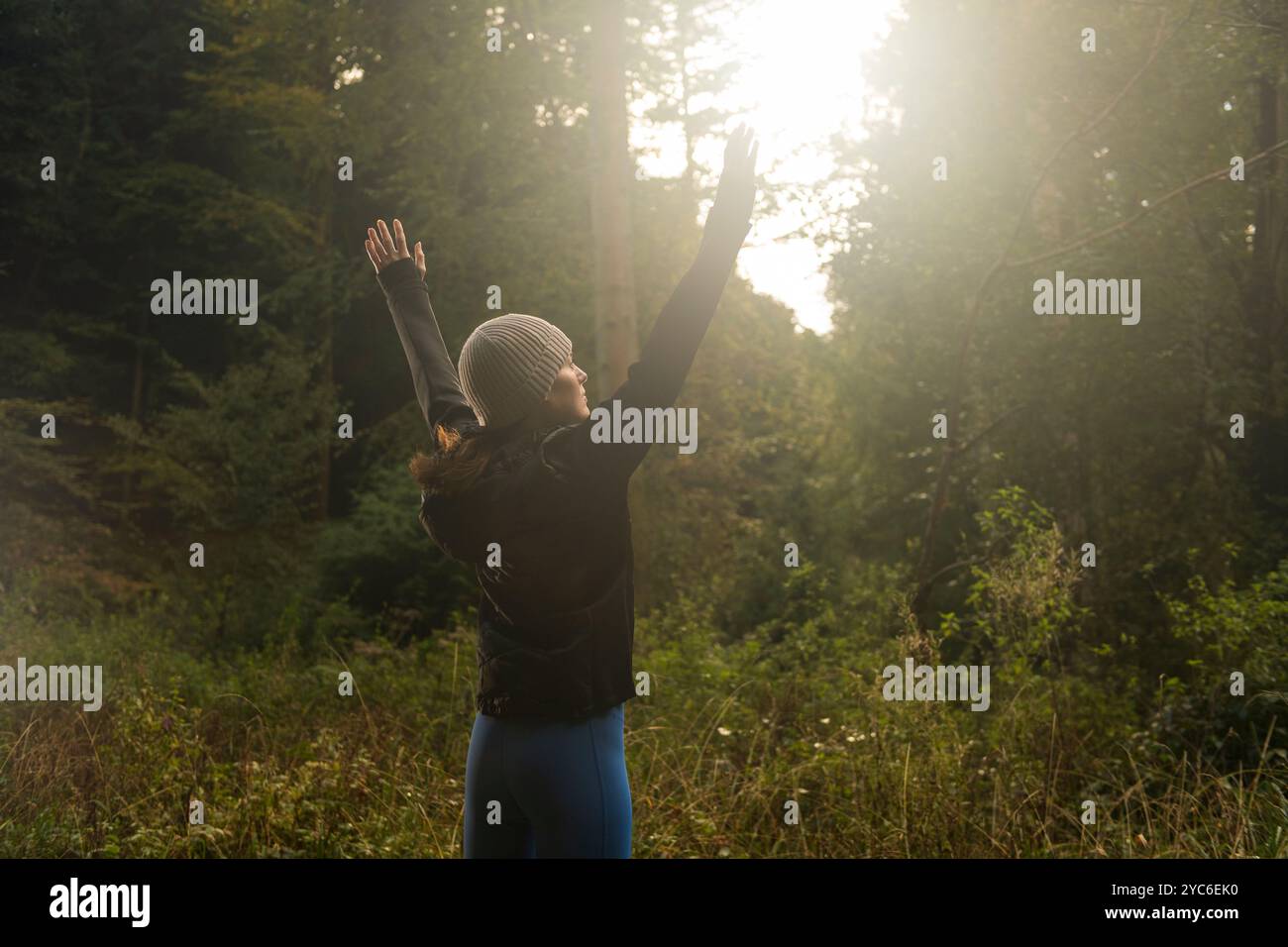 donna sportiva con le braccia alzate al sole. esercizio in una foresta. Foto Stock