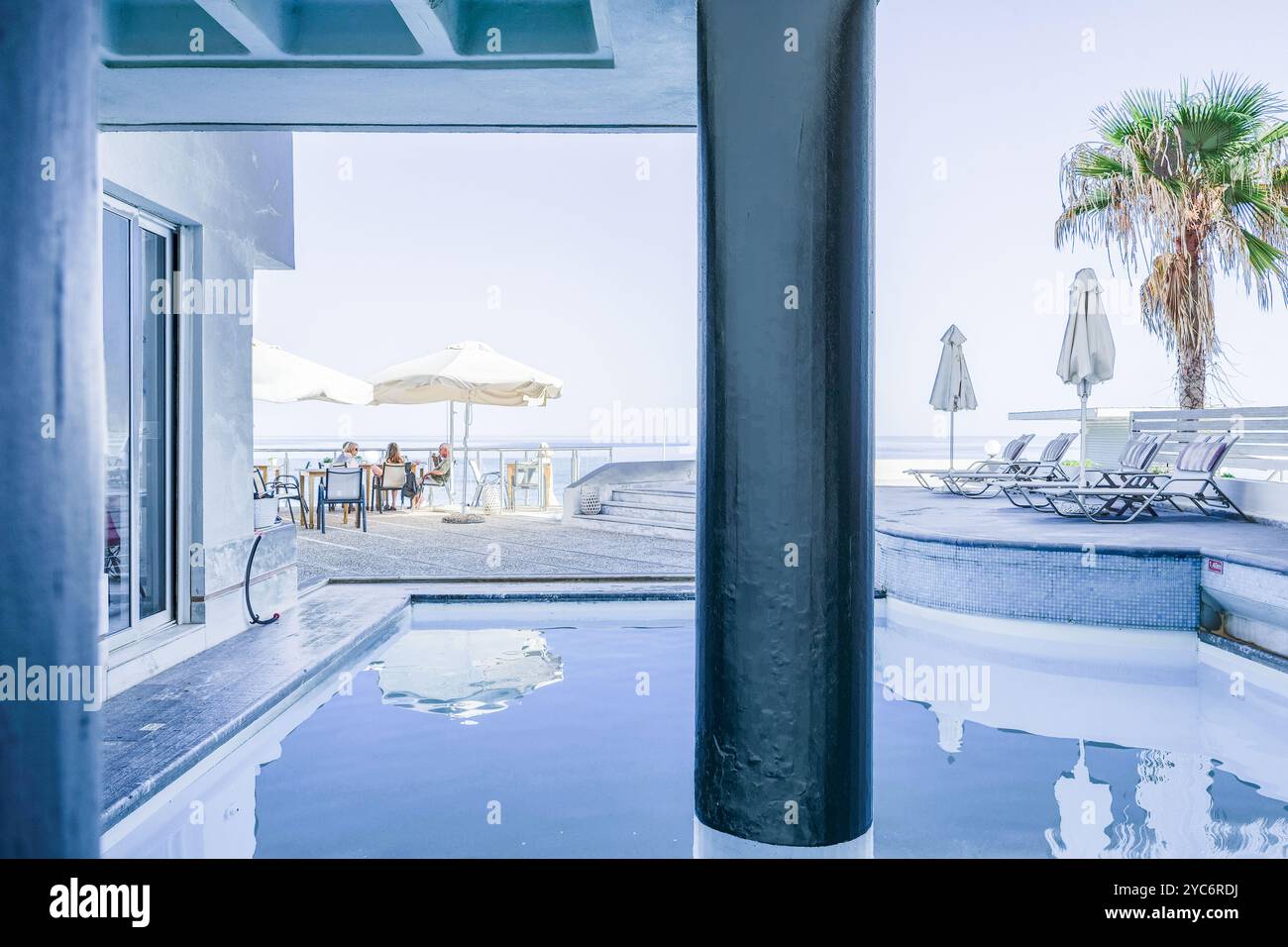 Una vista serena da un hotel a Rethymnon, Creta, Grecia, con particolare attenzione alla lussuosa area piscina e ai posti a sedere all'aperto. La scena include sedie a sdraio, Foto Stock