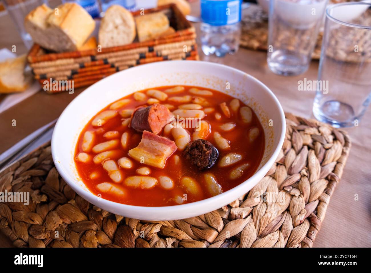 Una ciotola ripiena di Fabada asturiana, un tradizionale stufato spagnolo a base di fagioli e varie carni, siede su un tavolo di legno. Foto Stock