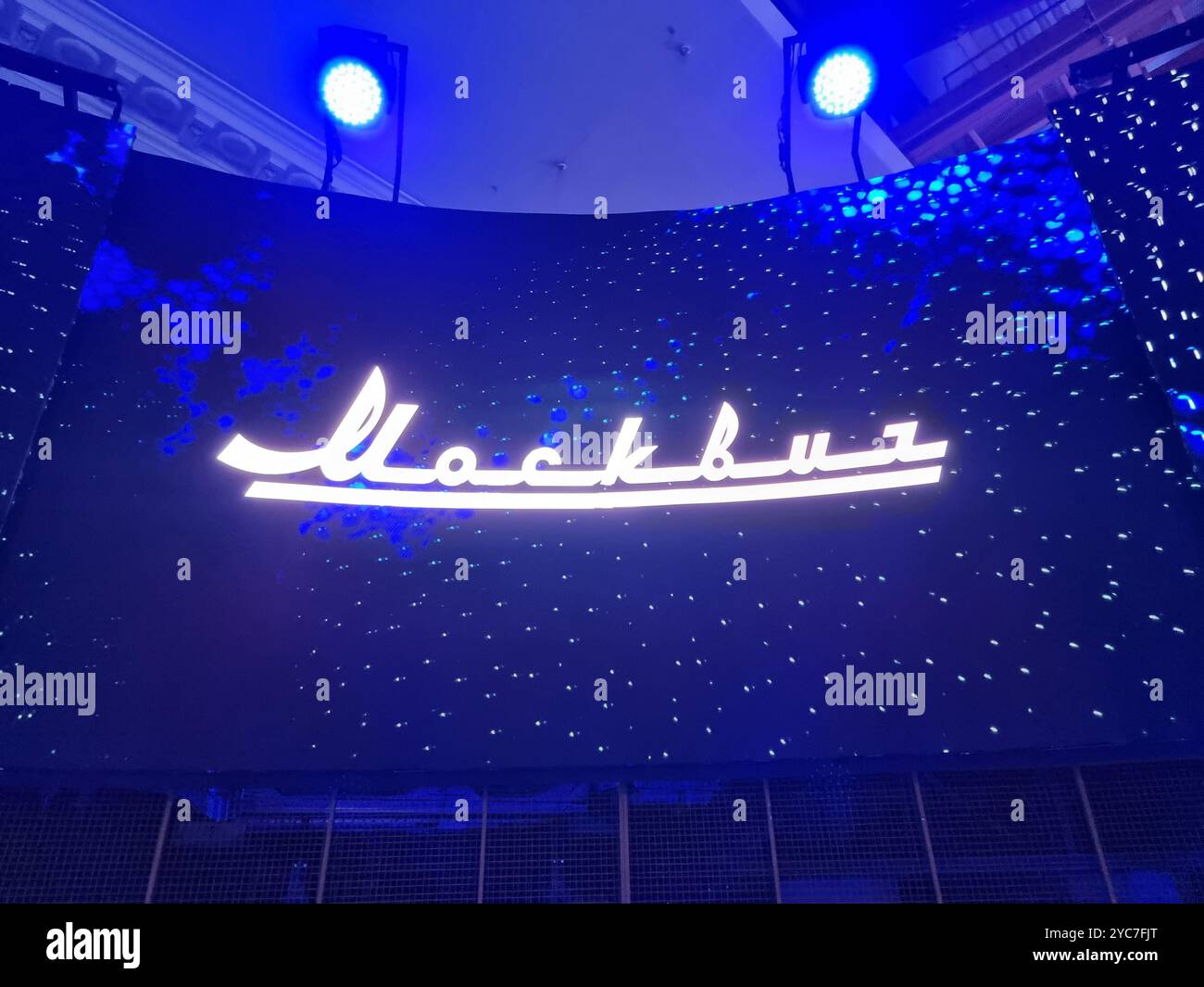 Grande proiezione del logo del marchio Moskvich su sfondo blu; marchio di automobili russo, marchio automobilistico, marchio automobilistico - Immagine stock catturata con smartphone