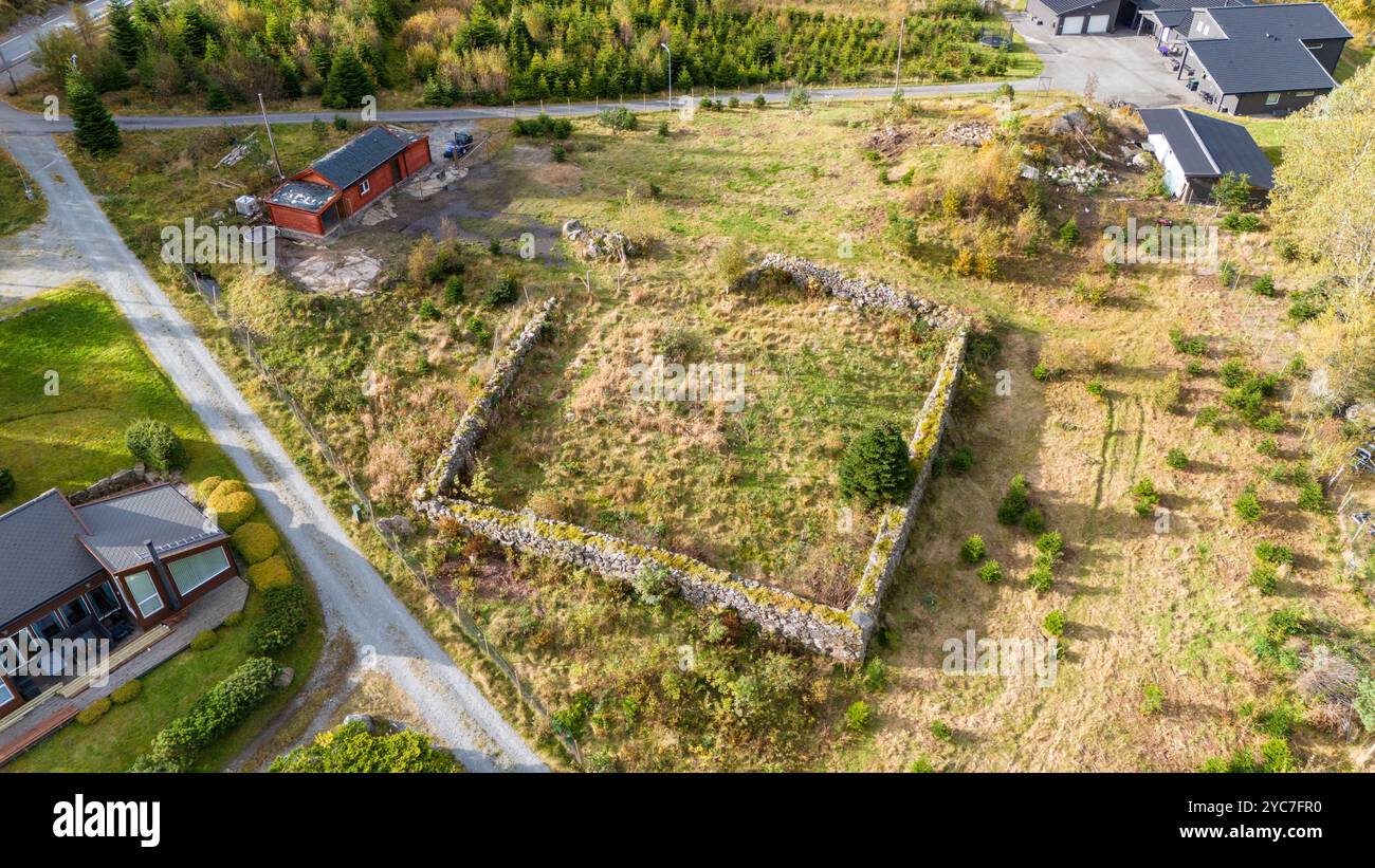 Vista aerea di un terreno vuoto circondato da vegetazione e strutture. La trama è segnata da un muro di pietra, con erba e arbusti sovradimensionati. Ne Foto Stock