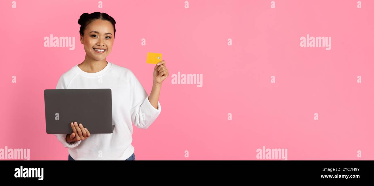 Giovane donna con un portatile e una carta di credito su sfondo rosa Foto Stock