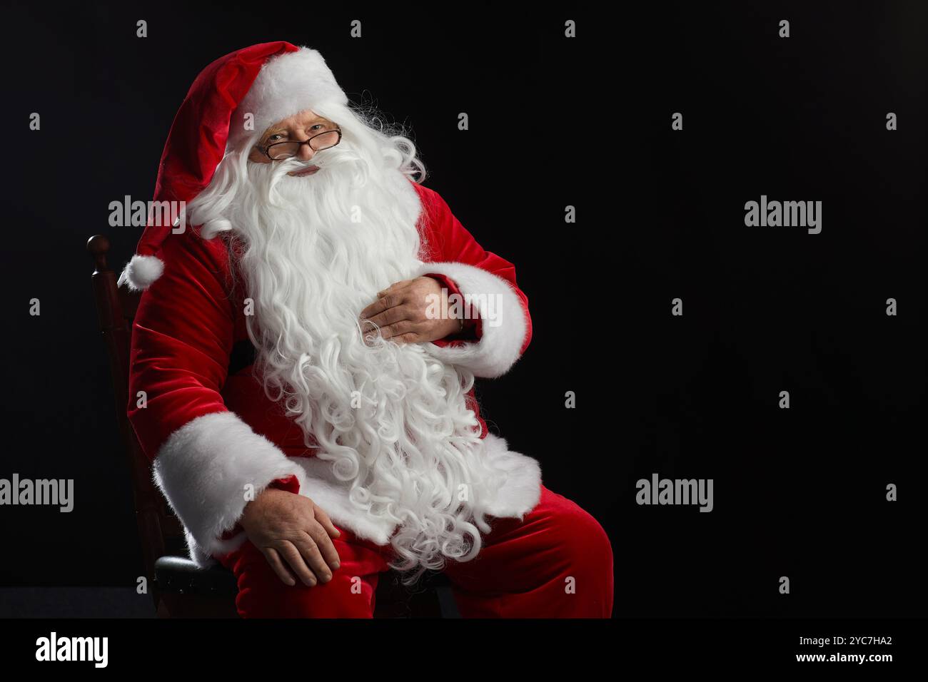 Babbo Natale si siede su uno sfondo nero e guarda la fotocamera. Natale, Capodanno, festeggiamenti natalizi, spazio per testo Foto Stock