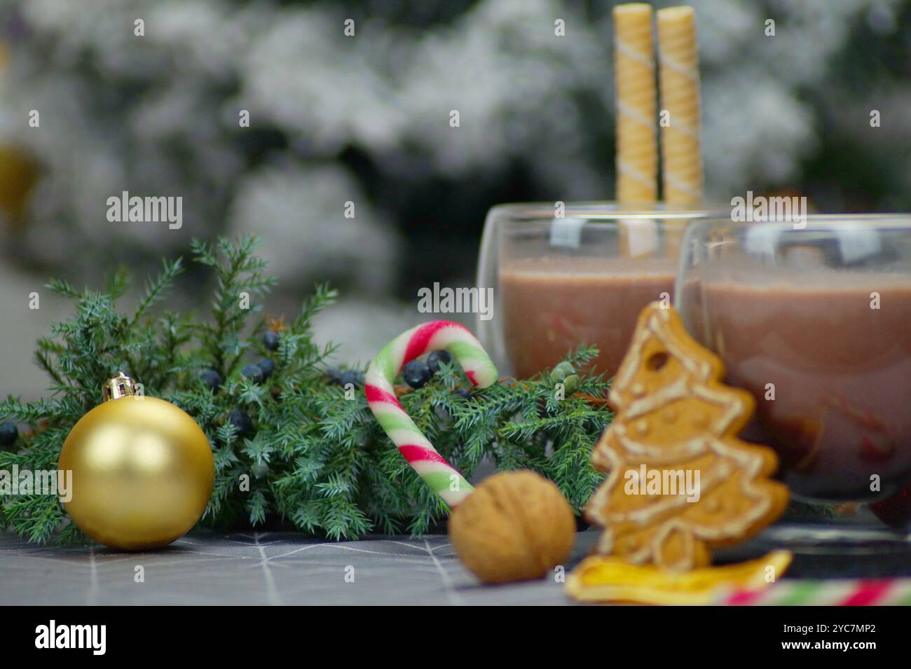 Una fotografia di Natale orizzontale che mostra due bicchieri di vetro trasparente riempiti di cioccolata calda. Bastoncini per waffle, bastoncini di caramelle, rami di pino, noci e anice Foto Stock