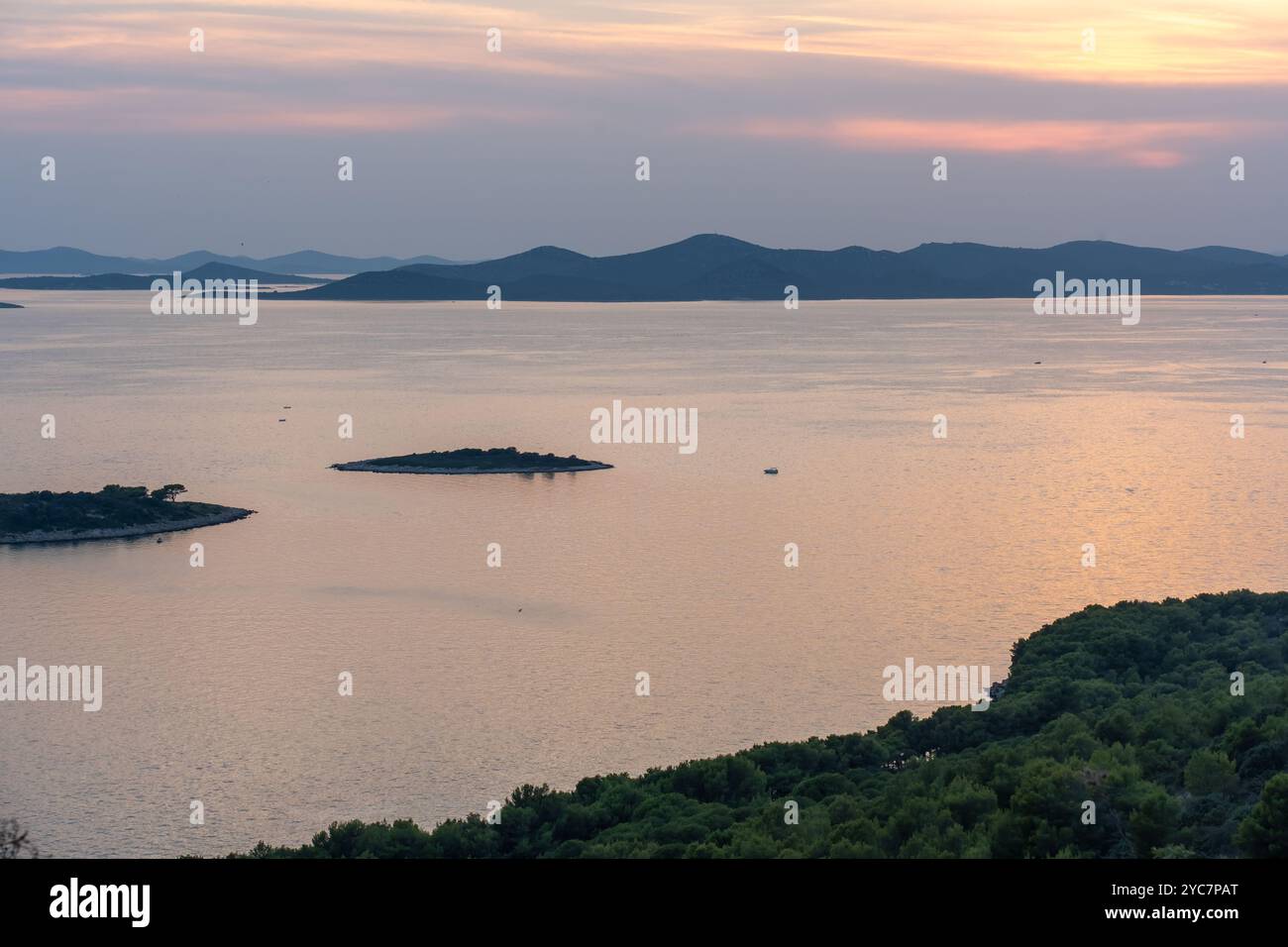 Tranquillo paesaggio costiero con mare calmo al tramonto e lontane isole verdi all'orizzonte. Foto Stock