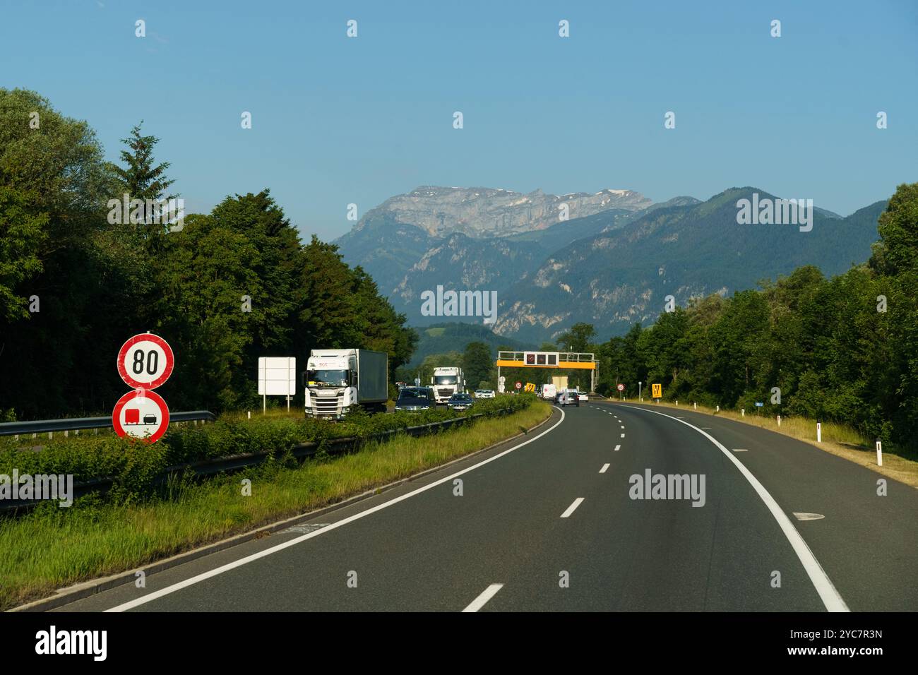 Jenbach, Austria - 13 giugno 2023: Una giornata limpida rivela uno splendido sfondo di montagna mentre i veicoli navigano sulla tortuosa autostrada circondata dalla lussureggiante greene Foto Stock