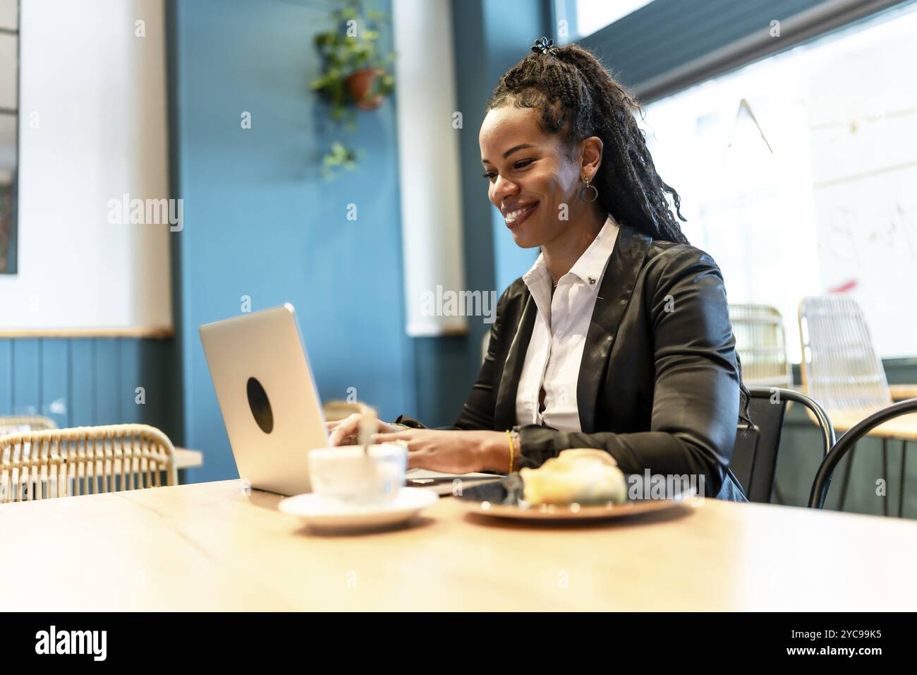 Donna d'affari latina che lavora con un computer portatile in una caffetteria mentre mangia un panino e beve un caffè Foto Stock