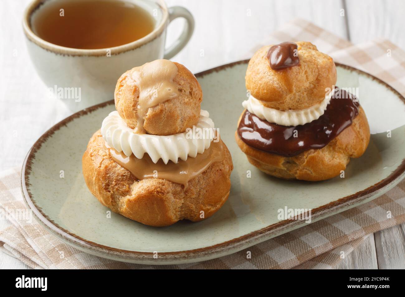 Religieuse Choux Buns ripieni di soffice crema alla vaniglia e glassa di cioccolato o caffè da vicino in una ciotola su un tavolo di legno. Orizzontale Foto Stock