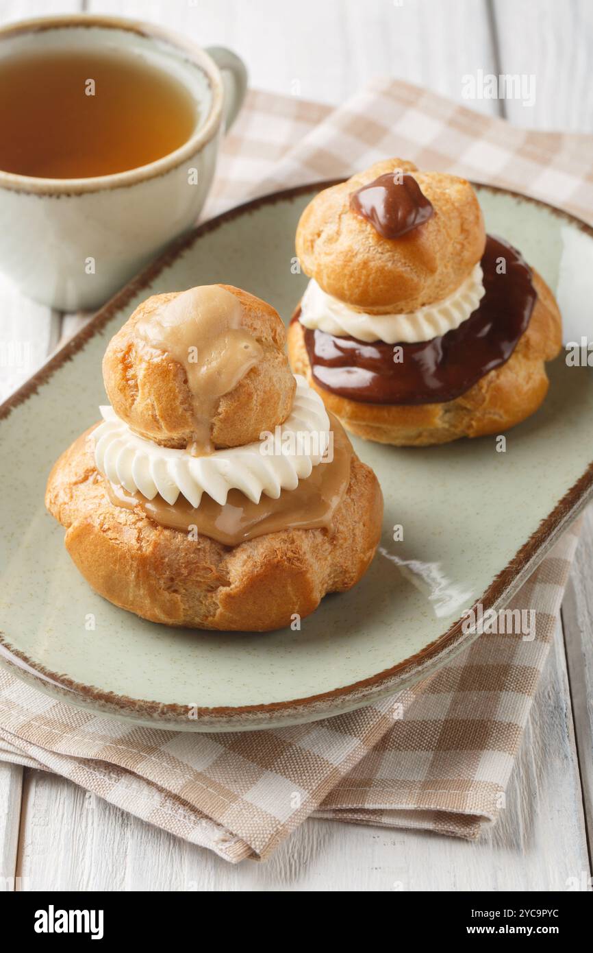 La pasticceria Religieuse è composta da due choux panini ripieni di crema pasticcera, ricoperti di ganache al cioccolato e decorati con il primo piano della crema sul piatto Foto Stock