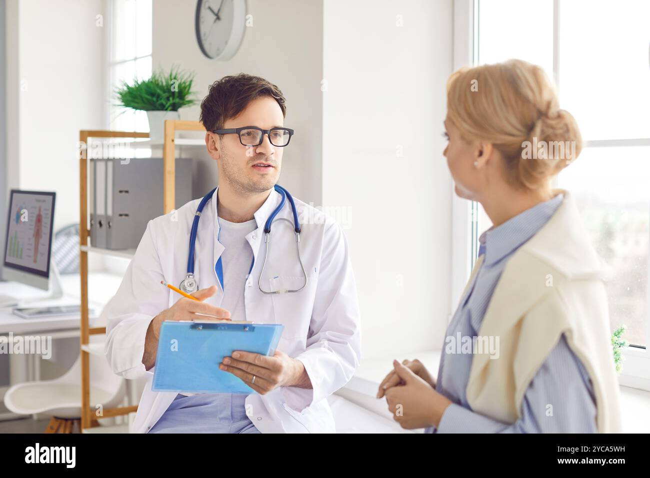 Giovane medico maschile che indossa uniforme medica bianca consulenza paziente femminile, parlando su consultazione Foto Stock