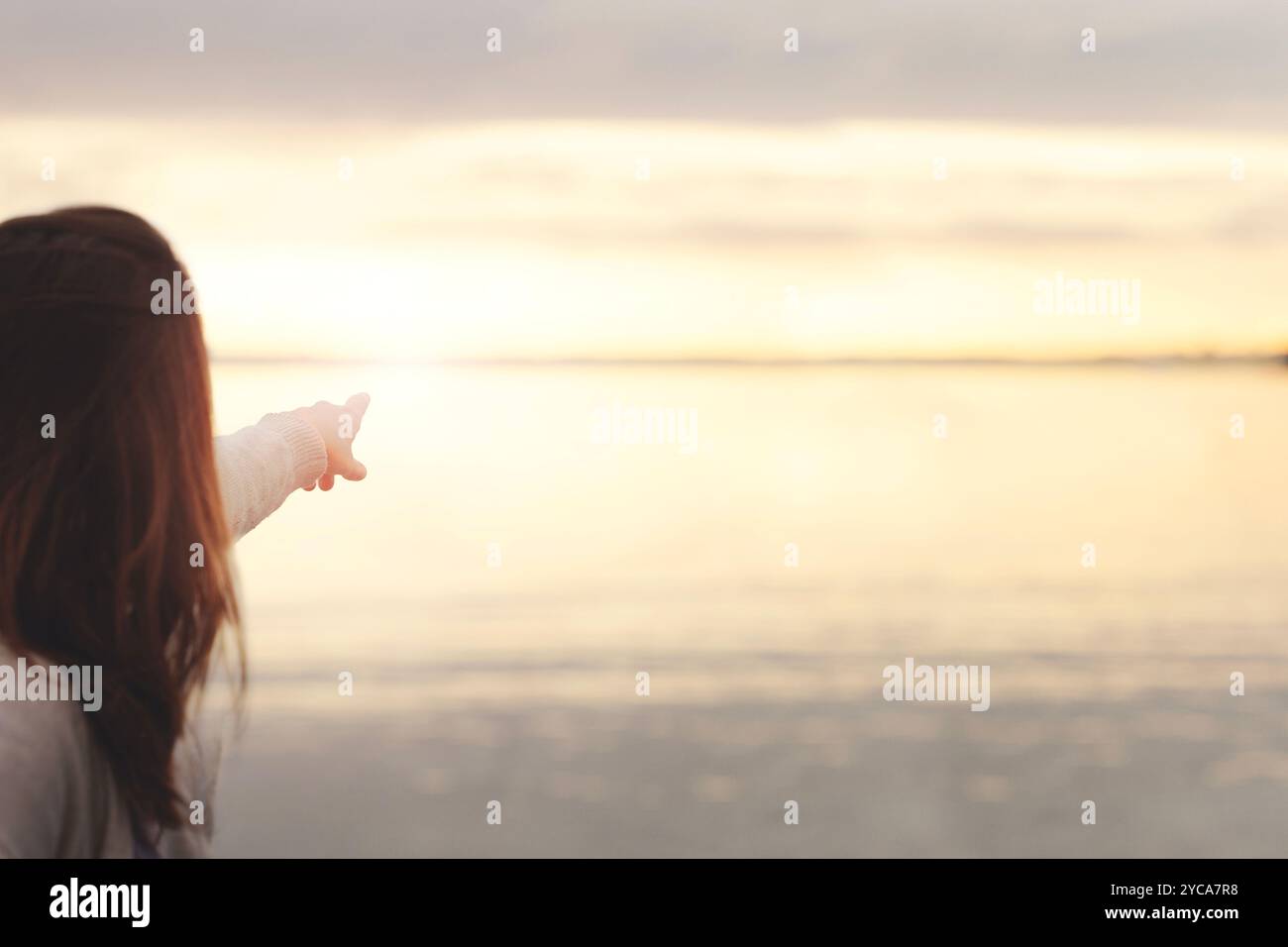 la persona punta con il dito il sole che tramonta sul mare, concetto di infinito e libertà Foto Stock