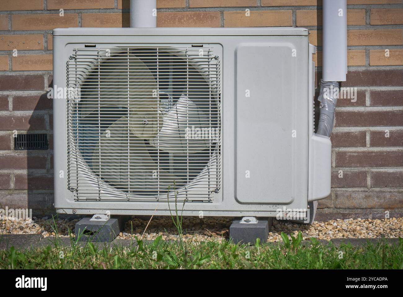 Moderna unità pompa di calore a sorgente d'aria montata all'esterno di una casa, contro una parete di mattoni, che dimostra una tecnologia a basso consumo energetico per il riscaldamento e il raffreddamento. Foto Stock