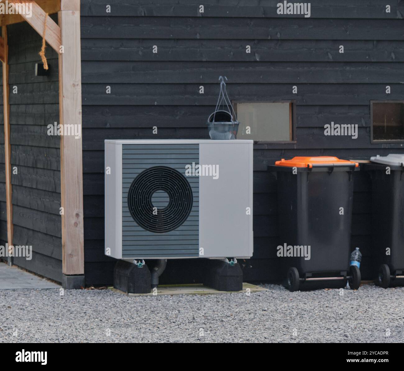 Moderna pompa di calore ad aria montata all'esterno di una casa, contro un garage a bordo, che dimostra una tecnologia efficiente dal punto di vista energetico per il riscaldamento. Foto Stock