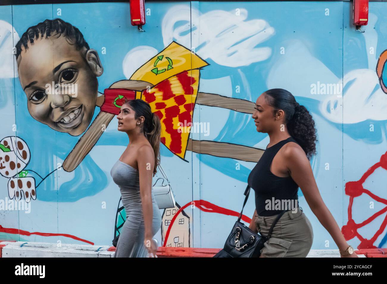 Inghilterra, Londra, Southwark, Two Girls Walking Beyond Colourful Billboard Foto Stock