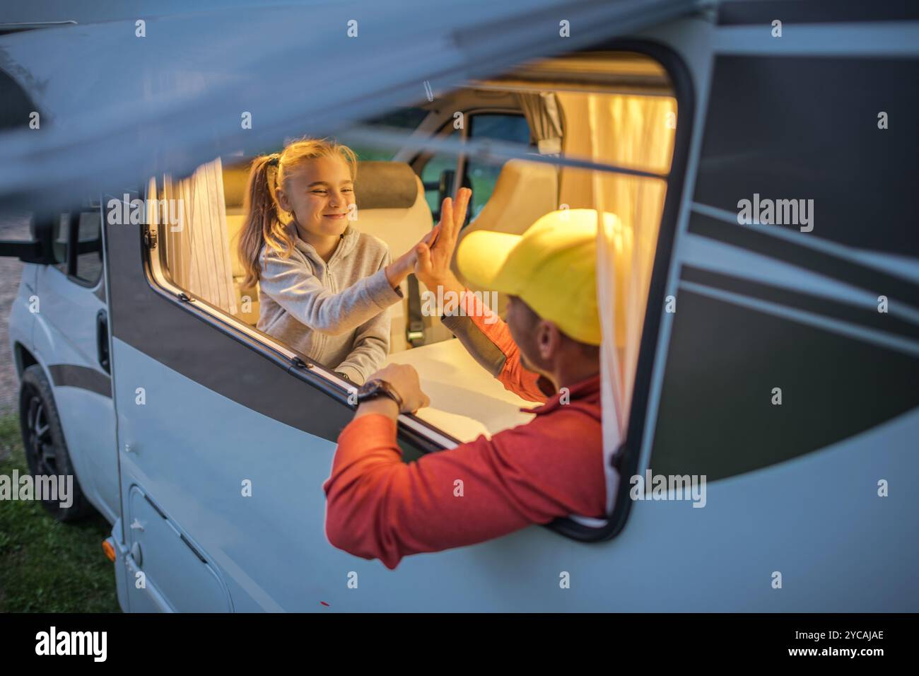 Un padre condivide un momento allegro con sua figlia mentre si godono del tempo di qualità insieme in un camper al crepuscolo, circondato dalla bellezza della natura. Foto Stock