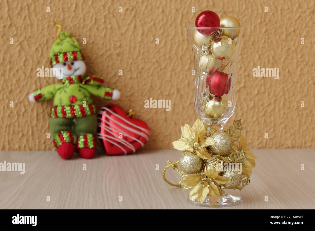 Sofisticato arredamento natalizio, con una tazza di cristallo riempita di palline rosse e dorate di Natale e un giocattolo imbottito di pupazzo di neve in un outfit di lana verde. Foto Stock