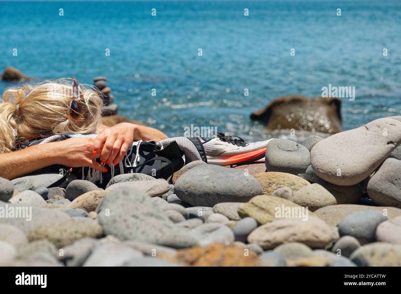 Donna bionda che riposa su una spiaggia di ciottoli, scarpe da running al suo fianco, Vereda da Ponta de São Lourenco Foto Stock
