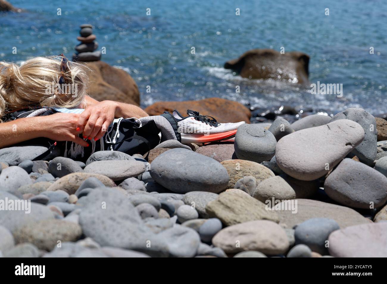 Donna bionda che riposa su una spiaggia di ciottoli, scarpe da running al suo fianco, Vereda da Ponta de São Lourenco Foto Stock