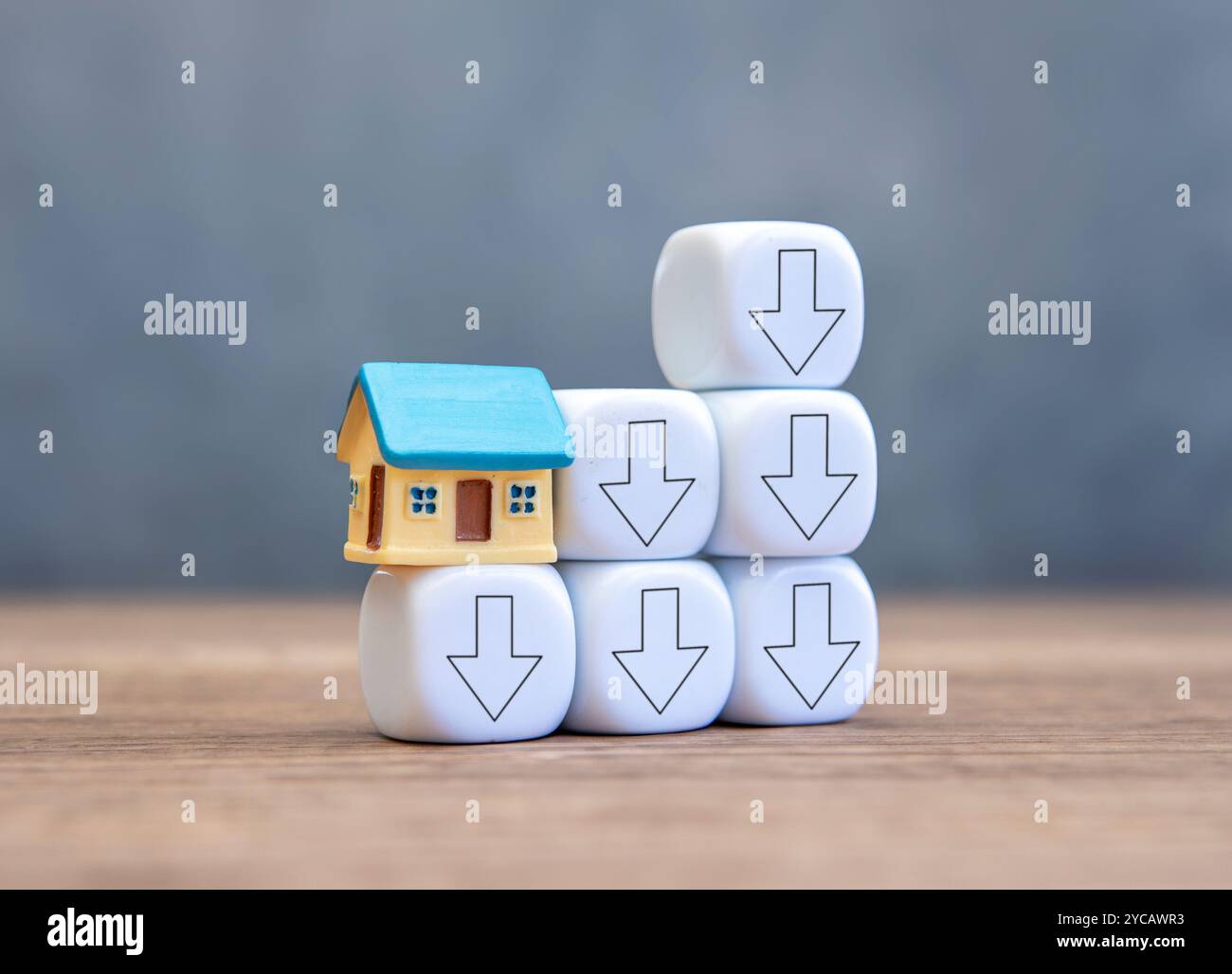 Una casa in miniatura in cima a un blocco bianco con frecce verso il basso. Mercato immobiliare, diminuzione dei prezzi e concetto di domanda. Foto Stock