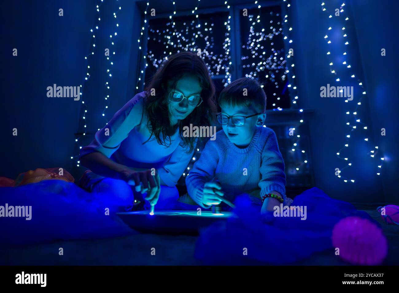 Bambino e terapista in camera stimolante sensoriale, Black snoezelen. Bambino autistico che gioca con il terapista durante la sessione di terapia occupazionale. Foto Stock