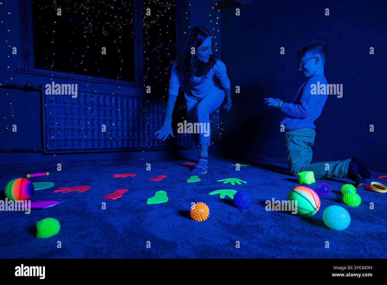 Bambino e terapista in camera stimolante sensoriale, Black snoezelen. Bambino autistico che gioca con il terapista durante la sessione di terapia occupazionale. Foto Stock