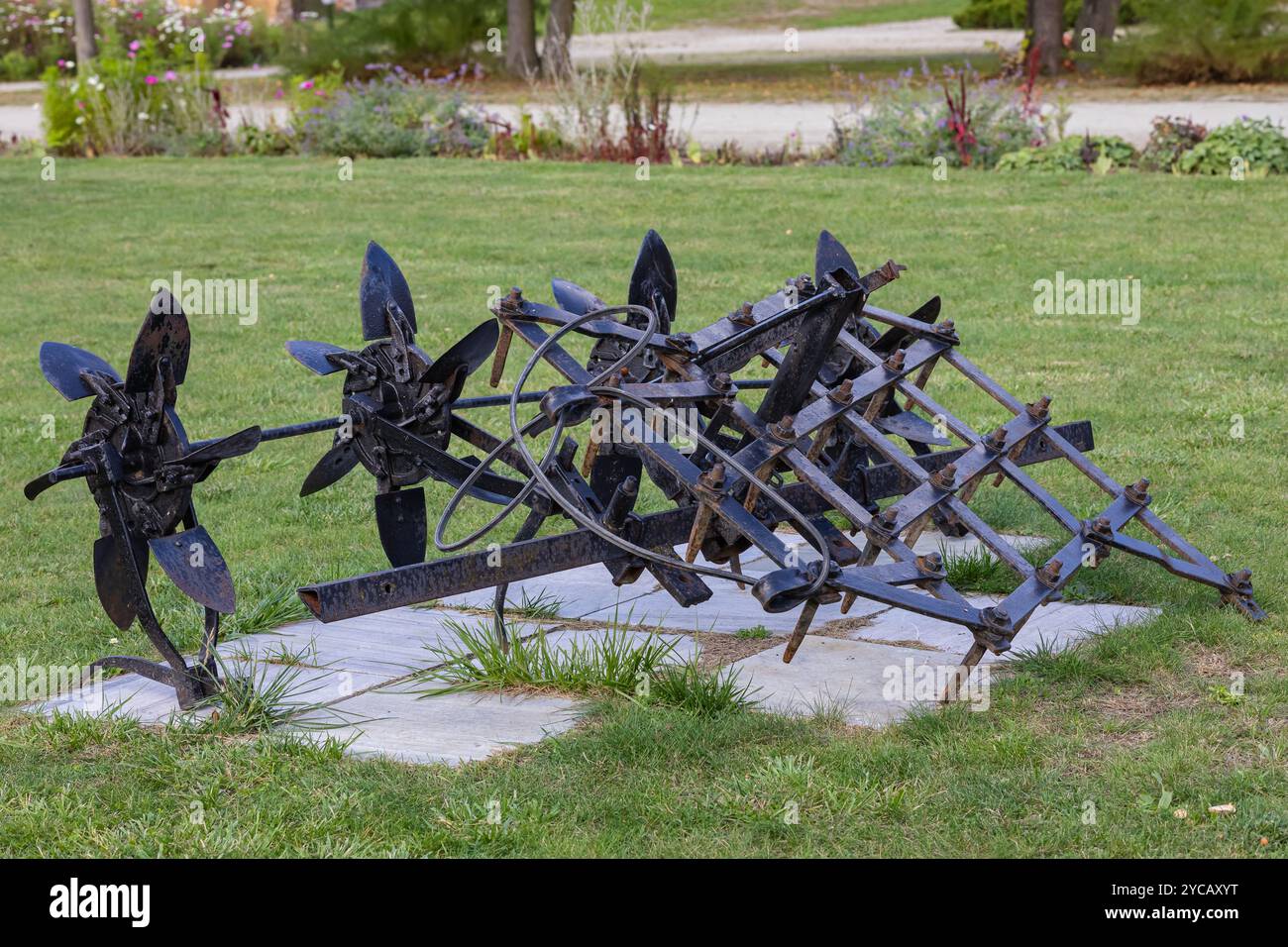 Vecchi macchinari agricoli arrugginiti esposti su prato verde nel parco. Concetto di strumenti agricoli d'epoca e attrezzature per lo stile di vita rurale Foto Stock