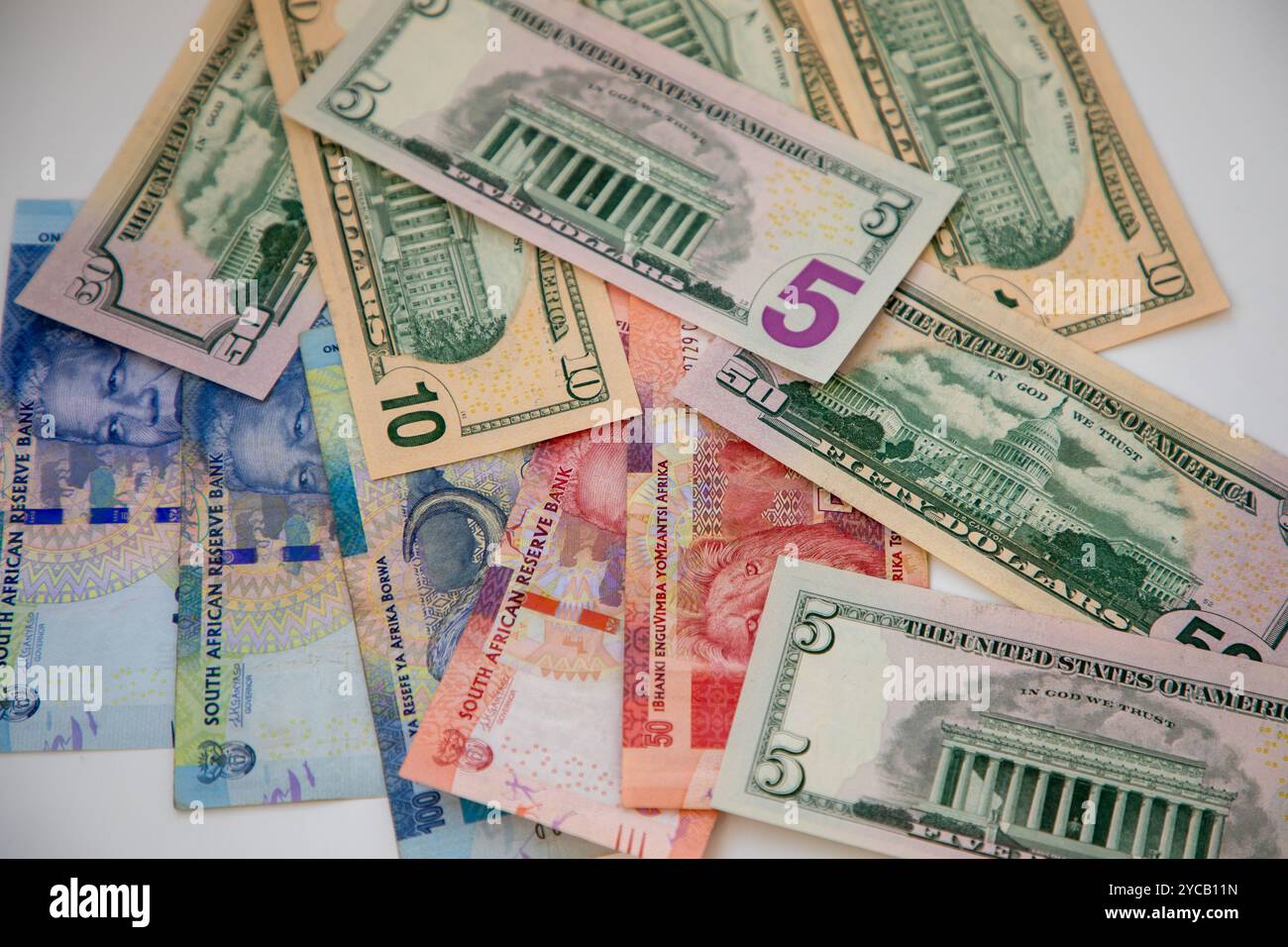 Varie denominazioni di banconote USA e banconote Rand sudafricane su sfondo bianco. Area di campo poco profonda. Foto Stock