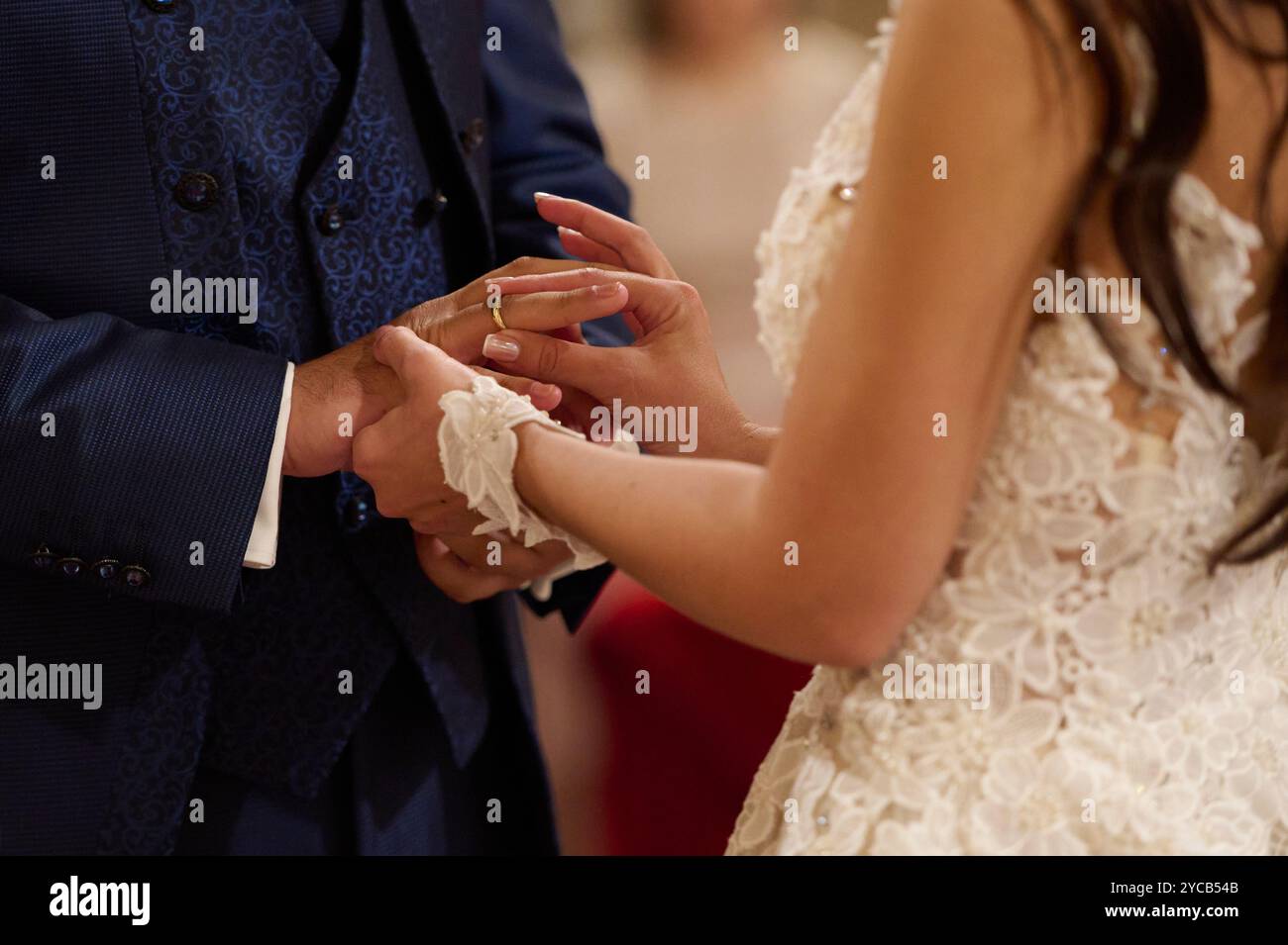 Uno scatto ravvicinato che cattura una sposa e uno sposo scambiando le fedi nuziali con una tuta blu fantasia posiziona delicatamente un anello sul dito della sposa Foto Stock