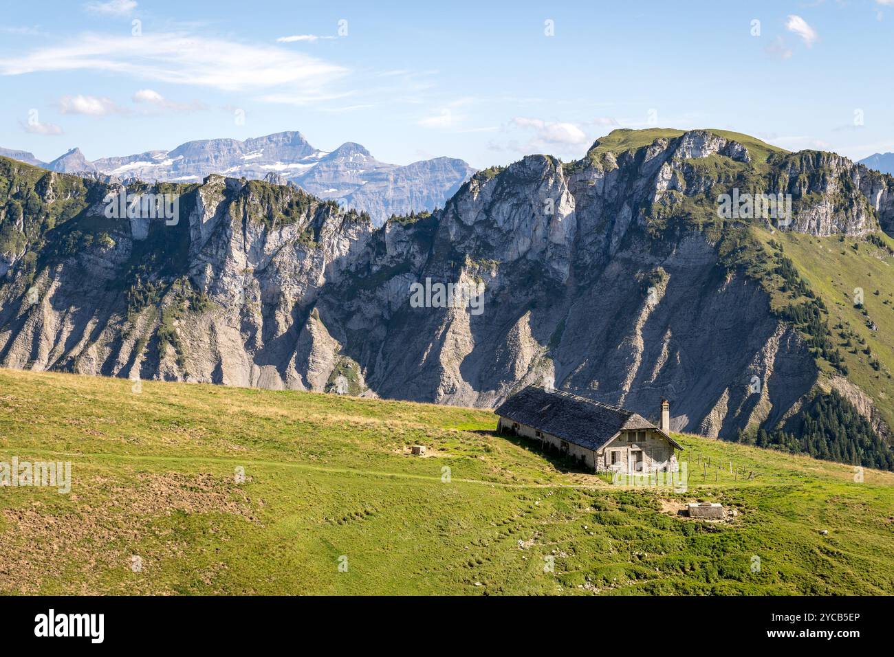 Una vista panoramica di una piccola cabina situata su pendii erbosi, affacciata su un tranquillo lago, circondata dalla maestosa area Rochers de Naye dell'Alpe Svizzera Foto Stock