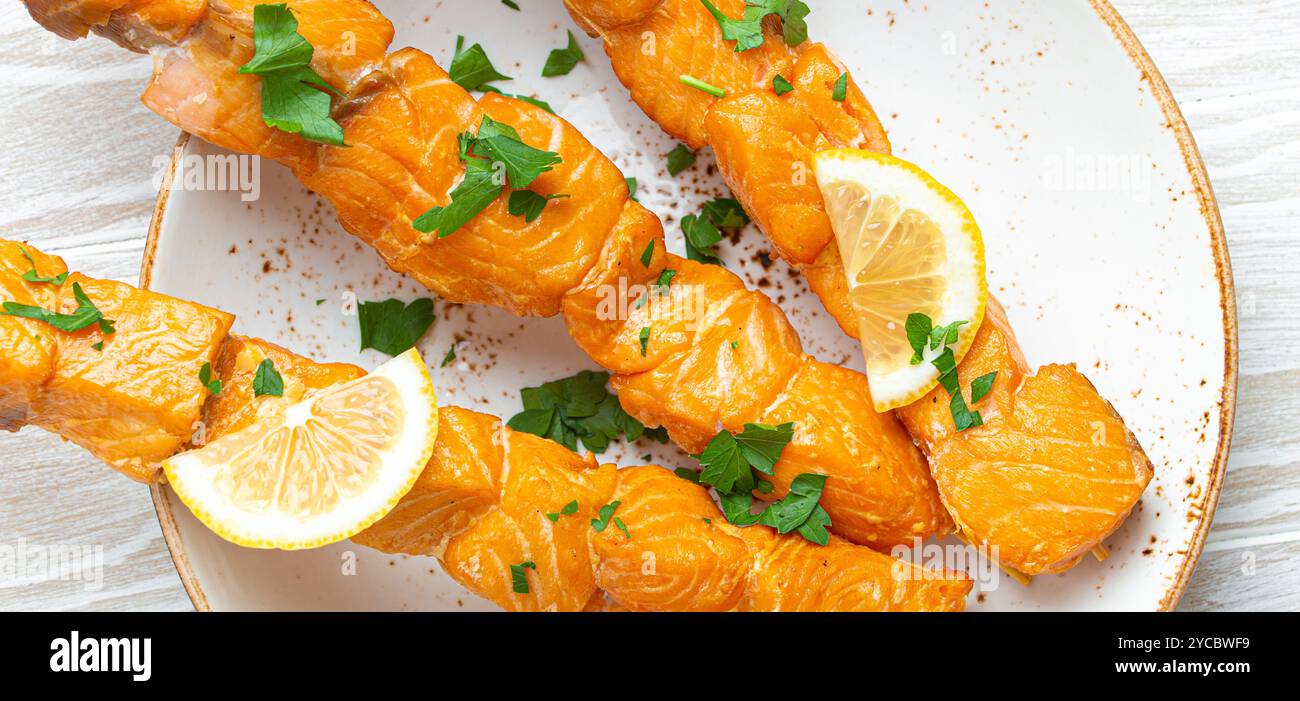 Spiedini di salmone alla griglia conditi con prezzemolo verde e limone su piatto di ceramica su tavola rustica in legno bianco vista dall'alto, salutare Foto Stock