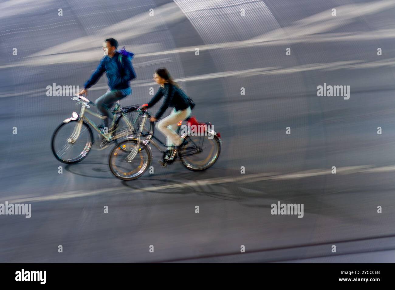 Un'immagine dinamica di una coppia in bicicletta per le strade della città di notte. La sfocatura in movimento cattura un senso di velocità e di vita urbana. Foto Stock