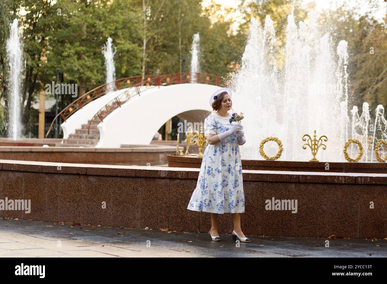 Una donna in abiti vintage e un cappello si staglia sullo sfondo di una fontana in un parco autunnale. Stile retrò Foto Stock