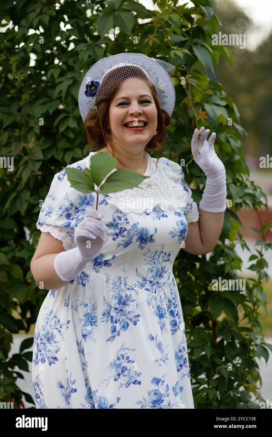 Una donna in abiti vintage e un cappello si staglia sullo sfondo di rami d'uva in un parco autunnale. Stile retrò Foto Stock