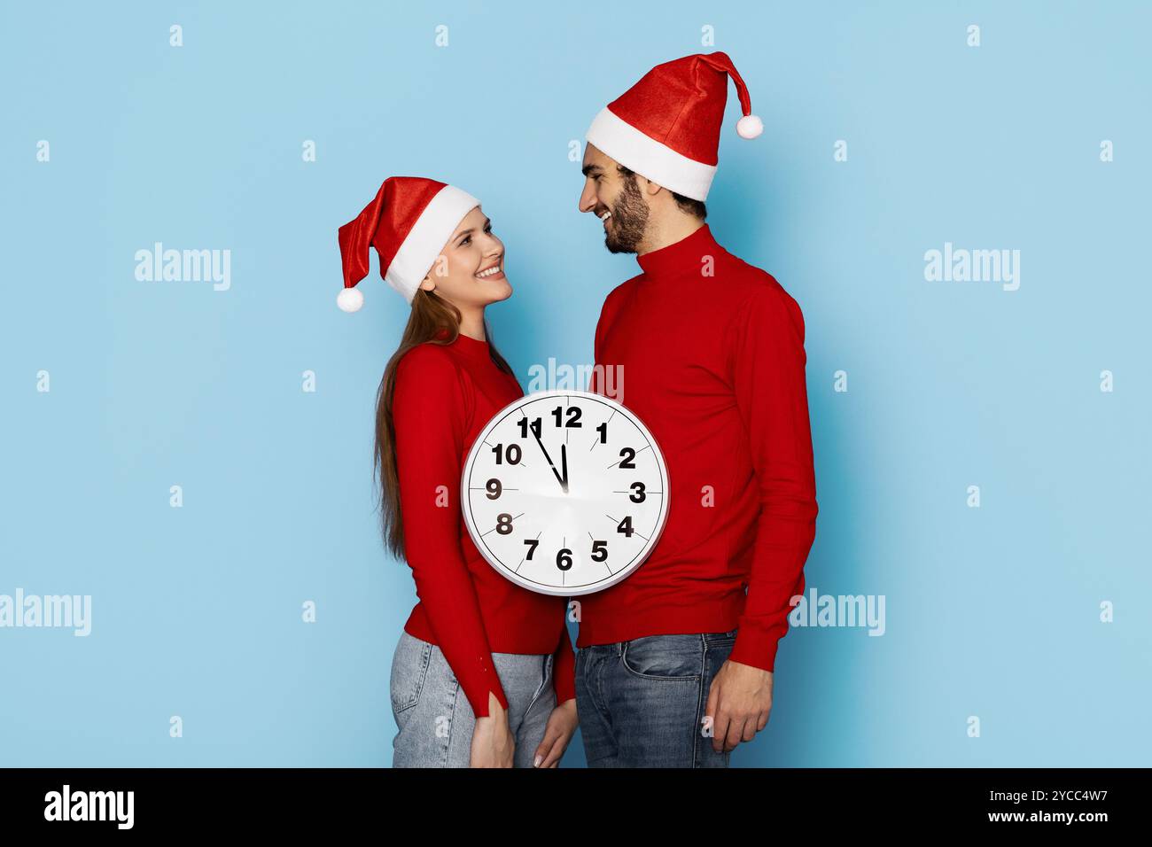 La coppia che indossa i cappelli di Natale sorride insieme a un orologio il giorno delle feste Foto Stock