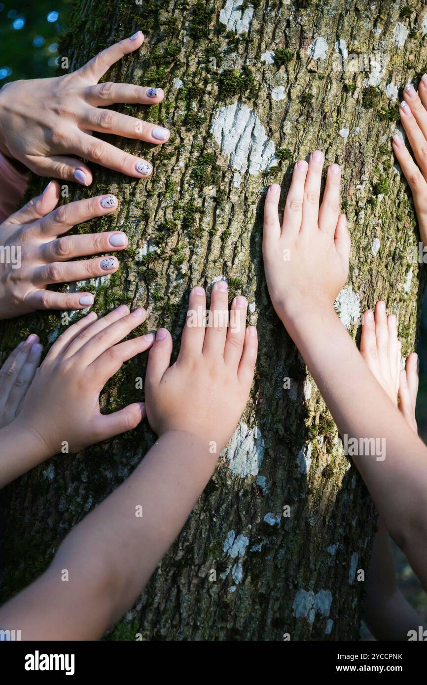 Un gruppo eterogeneo di individui in piedi insieme in natura, toccando delicatamente un albero vicino con le mani in un gesto armonioso Foto Stock
