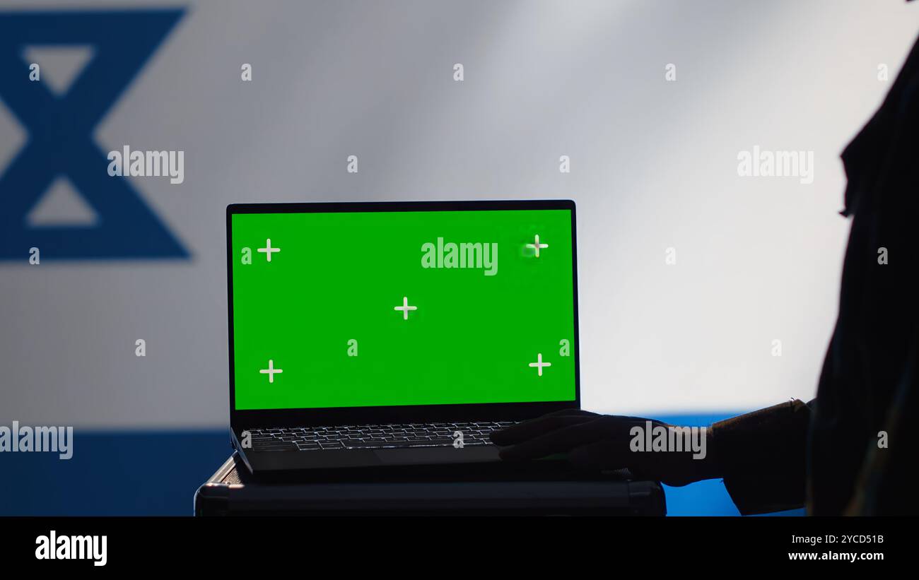 L'agente di polizia segreta di Israele utilizza strumenti di propaganda di massa su laptop con schermo verde per influenzare le menti della popolazione e diffondere disinformazione. La spia del Mossad commette il sabotaggio PsyOp utilizzando un notebook di mockup, la fotocamera A. Foto Stock
